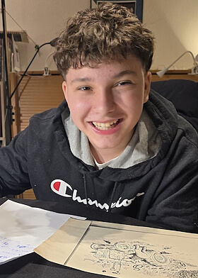 Zufriedener Schüler lächelt in die Kamera, während er in der Nachhilfe Deutsch an einer Aufgabe arbeitet.