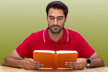 Erwachsener sitzt am Tisch und liest konzentriert in einem Buch – vertieftes Lernen innerhalb der Altersstufen.