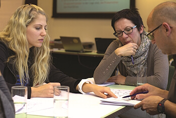 Zwei lernende Frauen diskutieren konzentriert mit dem Deutsch‑Lehrer über ein Thema – Privatunterricht Deutsch.