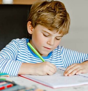 Ein Bub schreibt konzentriert mit einem Stift in sein Heft während der Nachhilfe Primarschule.