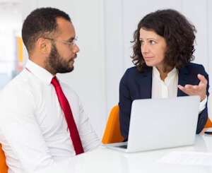 Mann und Frau sitzen nebeneinander am Arbeitstisch mit Computer und diskutieren im Privatunterricht Englisch.