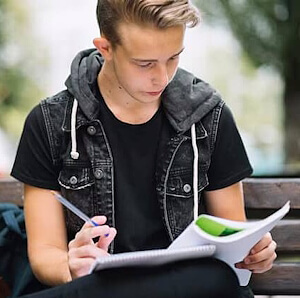 Matura‑Vorbereitung Bern – ein Gymnasiast liest draussen in einem Heft und macht sich Notizen.