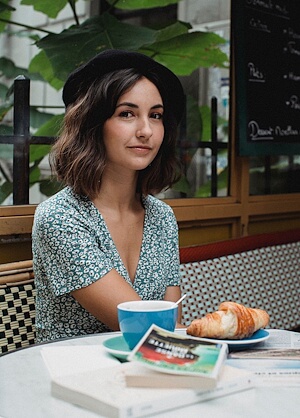 Frau sitzt entspannt in einem Pariser Café und geniesst Kaffee und ein Croissant.