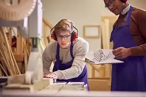 Berufsfachschüler in der Ausbildung zum Schreiner EFZ bekommt vom Lehrmeister an der Kreissäge Instruktionen; Bild für die Nachhilfe Berufsfachschule.