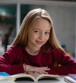 Ein Mädchen sitzt vor einem Buch in der Nachhilfe Primarschule und schaut in die Kamera.
