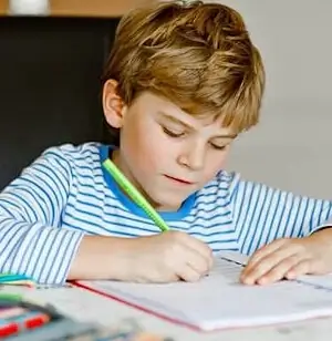 Ein Bub schreibt konzentriert mit einem Stift in sein Heft während der Nachhilfe Primarschule.